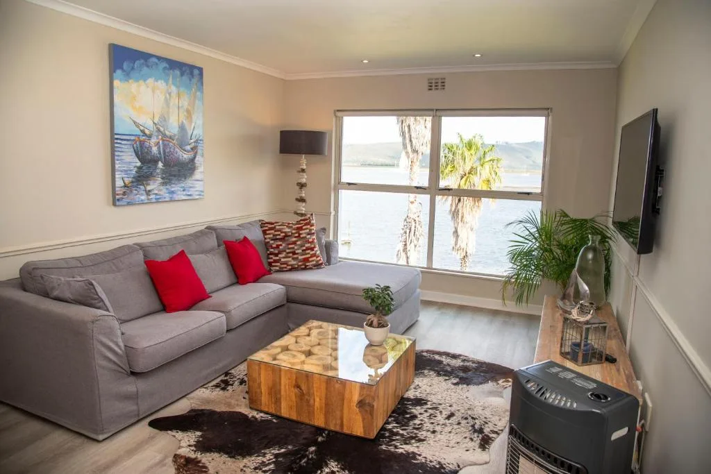 Comfortable gray sofa with red cushions overlooking lagoon through large windows