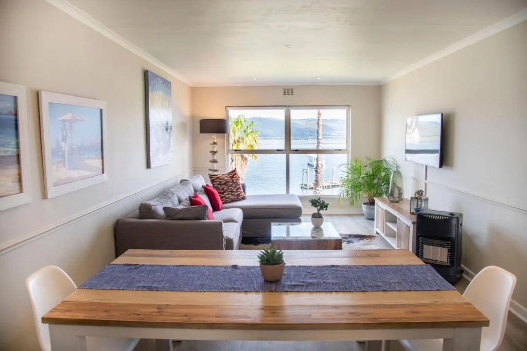Open-plan lounge with gray sofa, dining table, and lagoon views through large windows