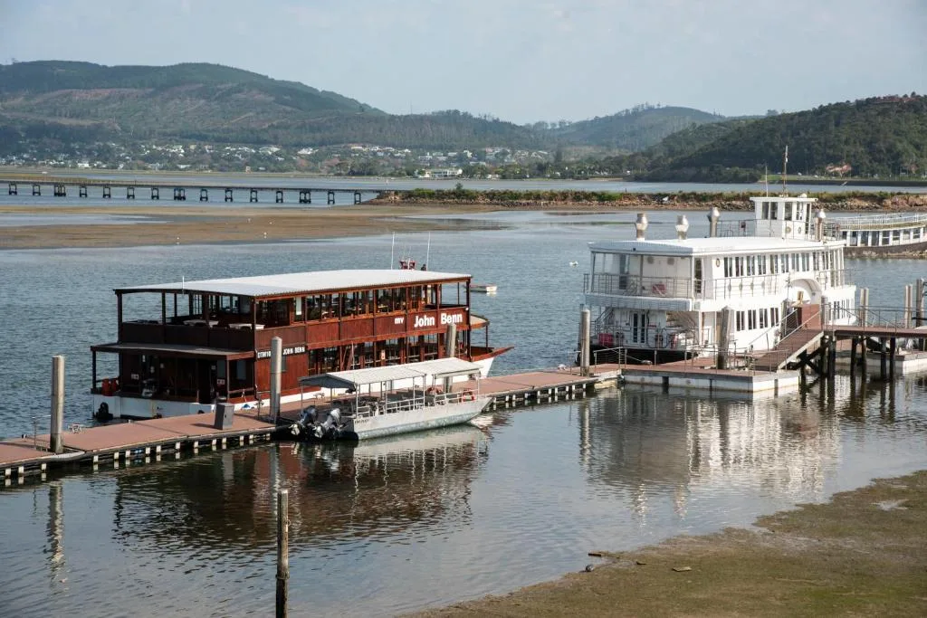 Knysna lagoon waterfront with boats, bridge, and forested mountains beyond