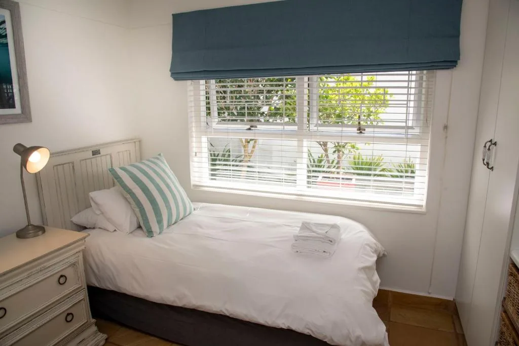 Bright bedroom with white bedding, green striped pillow, and garden views