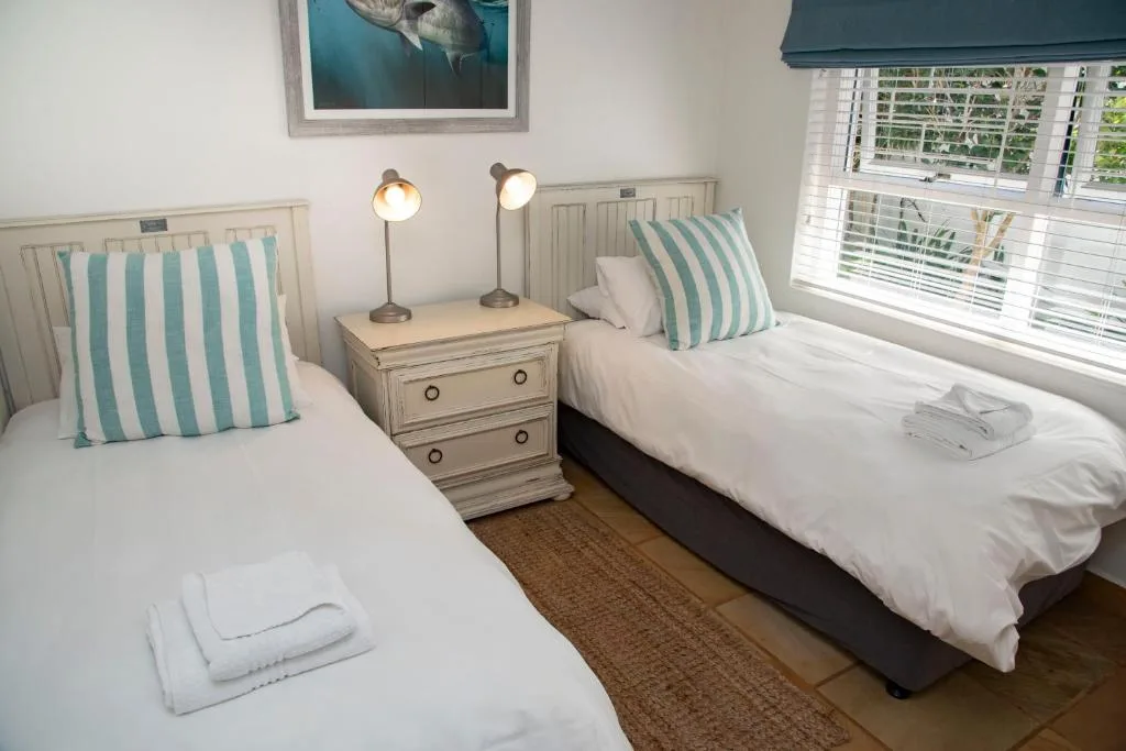 Twin beds with striped pillows, bedside table with lamps, bright windows