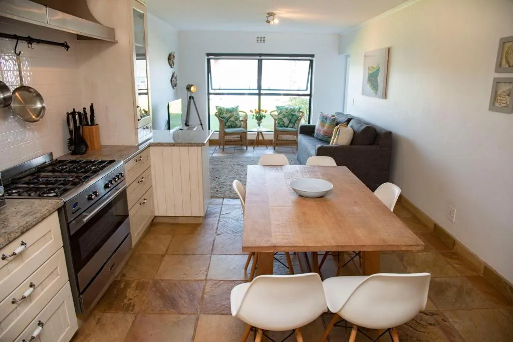 Open-plan dining area with wooden table and white chairs, kitchen visible