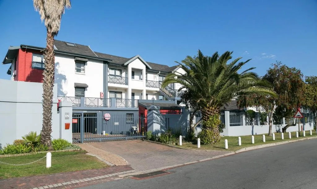 Modern apartment building with red accents, palm trees, and brick driveway entrance
