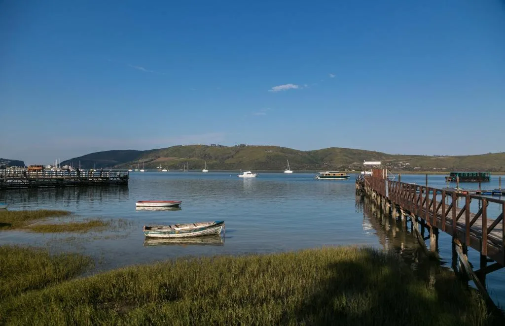 Scenic waterfront view of Knysna Lagoon with moored boats and green hills