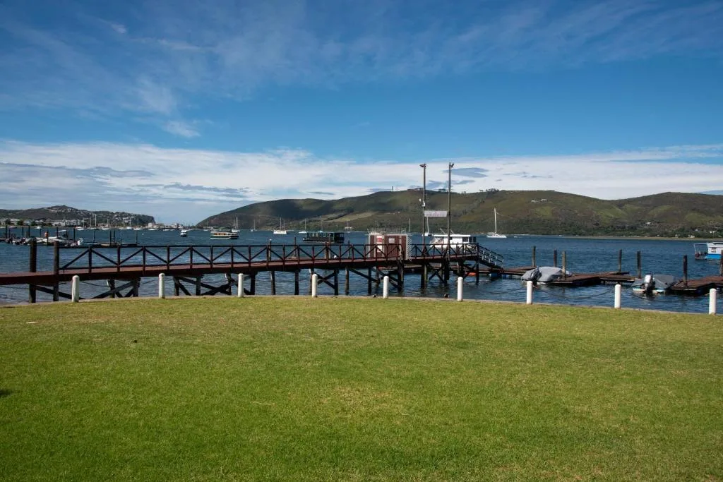 Scenic lagoon view with jetty, boats, and green hills across water