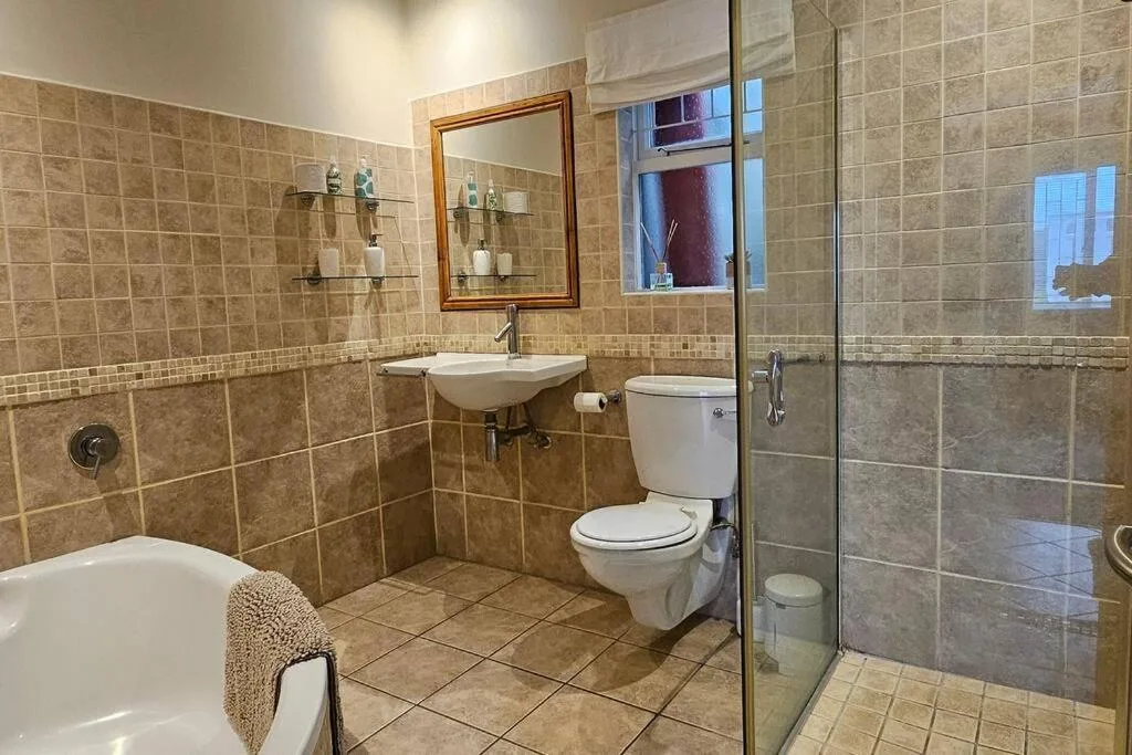Spacious bathroom with tiled walls, walk-in shower, toilet and vanity sink