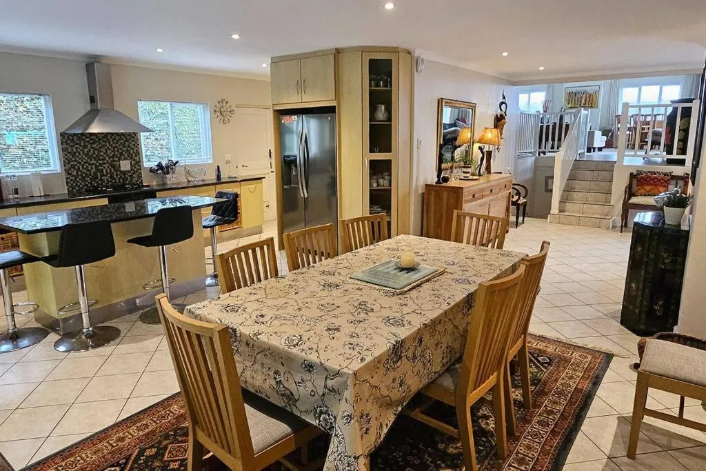 Spacious dining area with wooden chairs and patterned tablecloth, open-plan kitchen visible