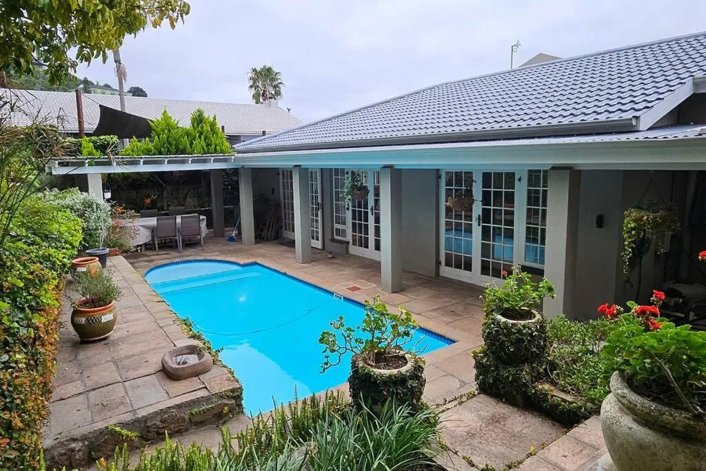 Bright blue swimming pool surrounded by lush garden and covered patio area