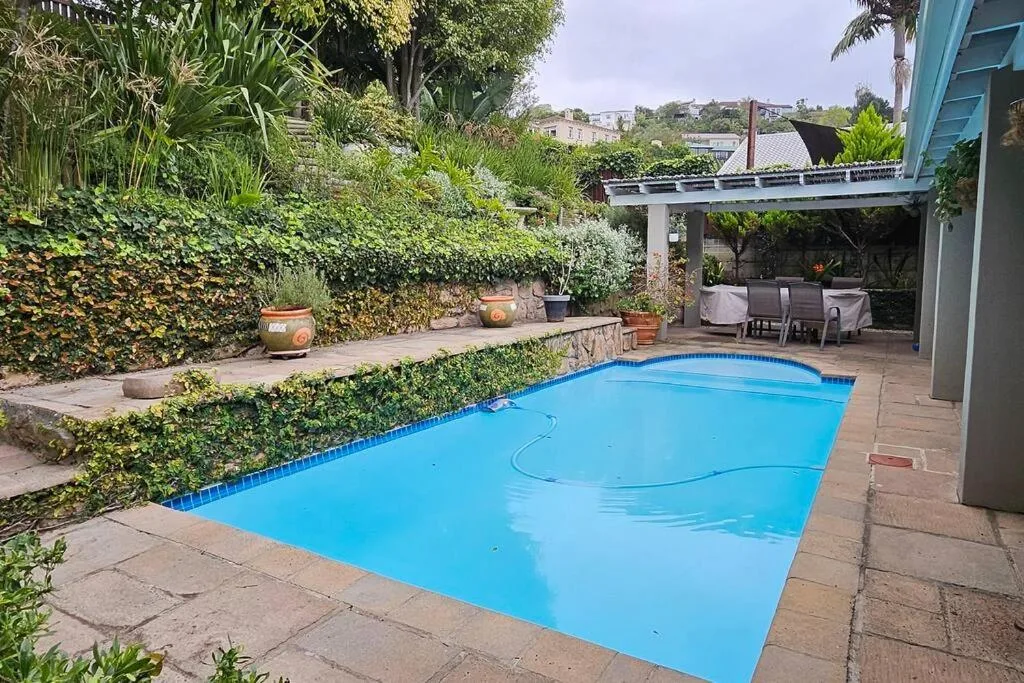 Bright blue rectangular swimming pool surrounded by lush gardens and patio seating