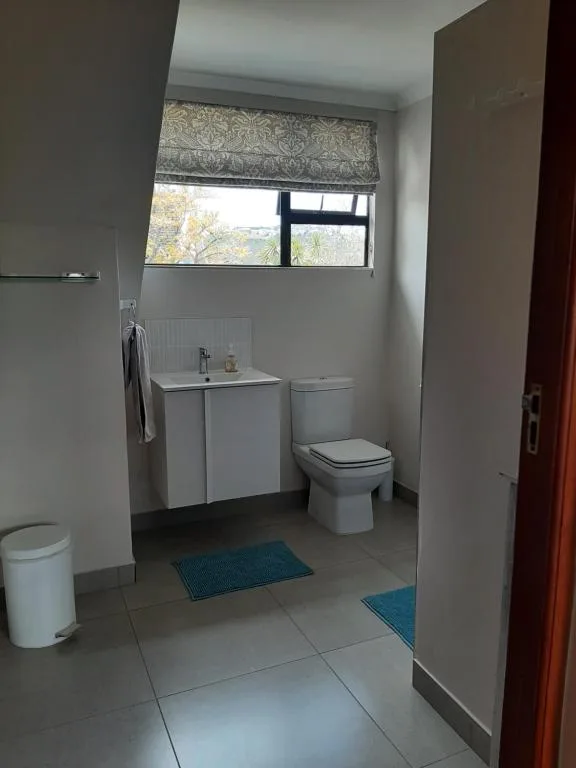 Clean bathroom with white vanity, toilet, and window with patterned blind