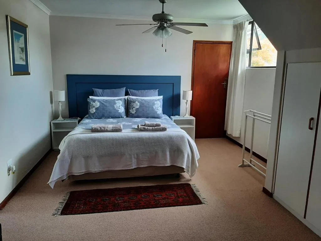 Spacious bedroom with blue headboard bed and cream bedding, ceiling fan