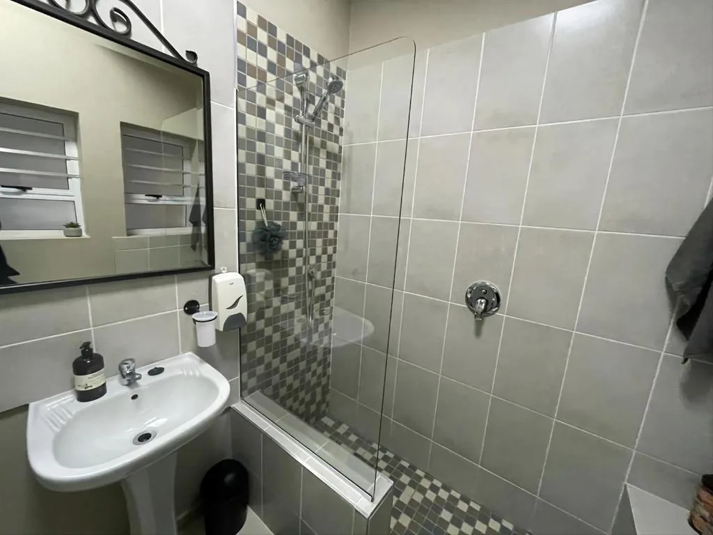 Modern bathroom with white tile walls, pedestal sink, and glass shower enclosure