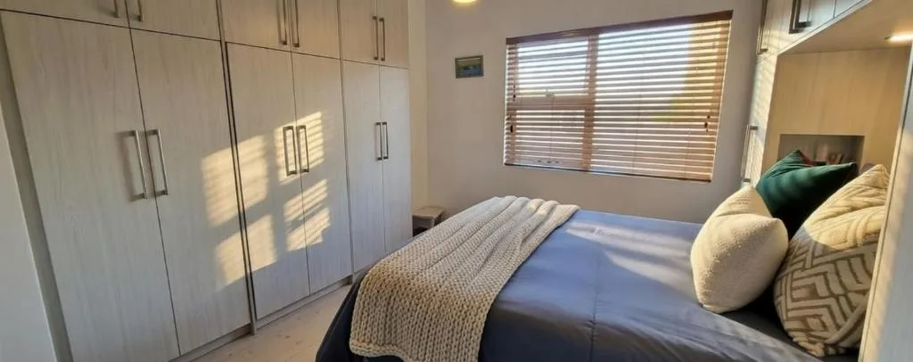 Modern bedroom with double bed, white built-in wardrobes, and bright windows