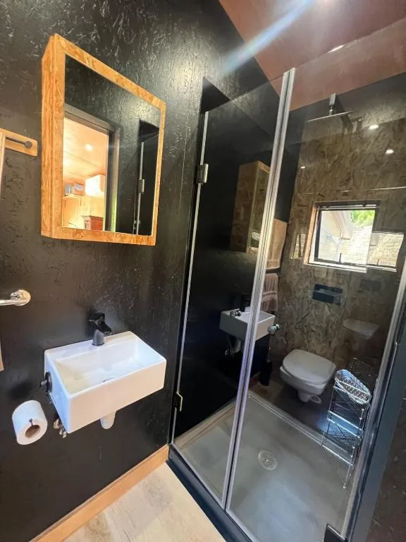 Modern bathroom with dark walls, white sink, wooden mirror frame, and glass shower enclosure