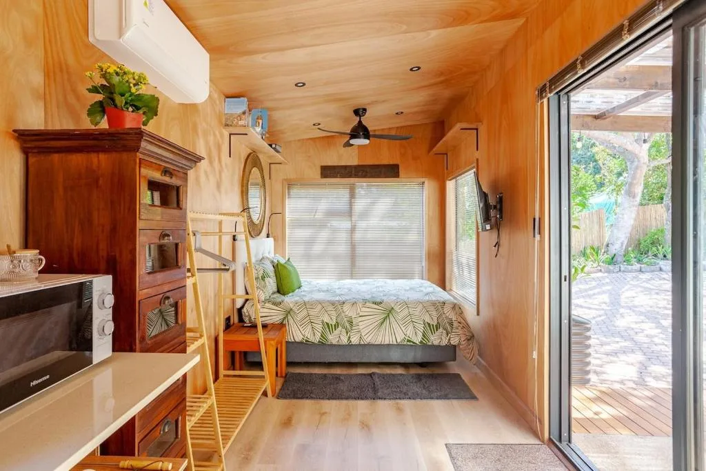 Compact bedroom with queen bed and wooden finishes, opening to deck