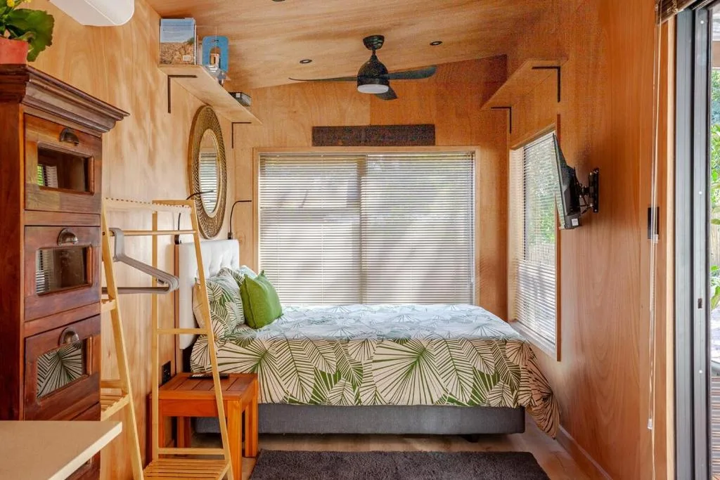 Cozy bedroom with queen bed, wooden walls, and lagoon views through large windows