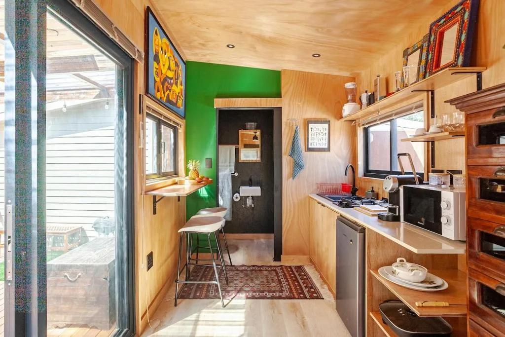 Compact kitchen with wooden cabinetry, stove, and colorful green accent wall