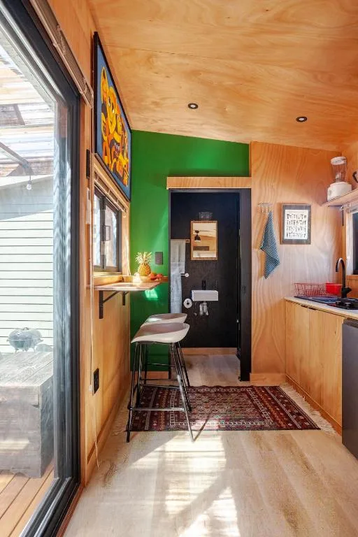 Compact kitchen with wooden cabinets, green accent wall, and natural light