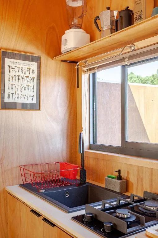 Compact wooden kitchen with gas cooktop, sink, and open shelving displaying kettle