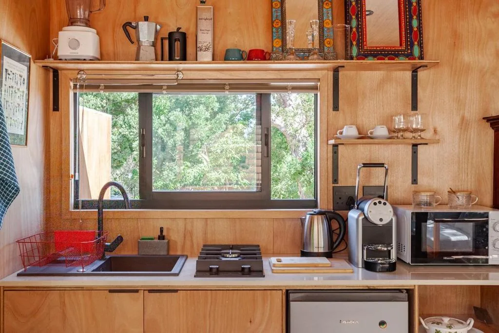 Compact kitchen with wooden cabinetry, stovetop, and large window overlooking trees