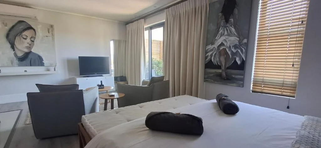 Modern bedroom with white bed, TV, lounge seating, and contemporary artwork