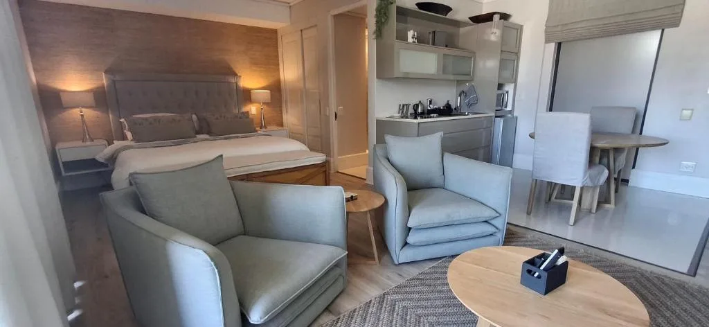 Modern bedroom with upholstered bed, seating area, and open-plan kitchen behind