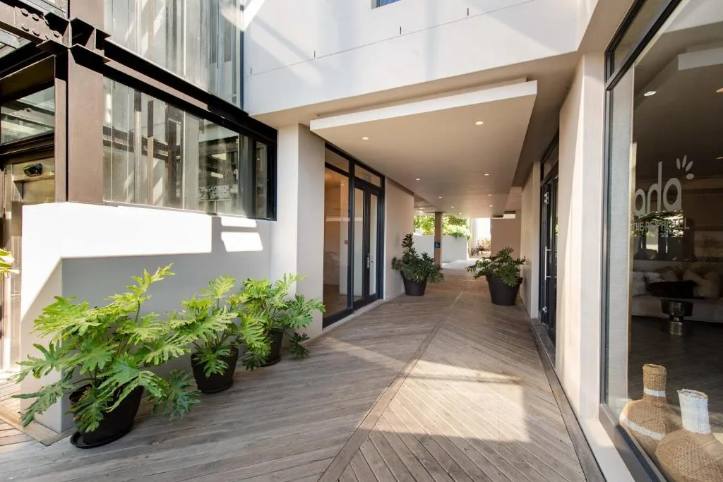 Modern covered deck with wooden flooring and potted plants, leading to interior