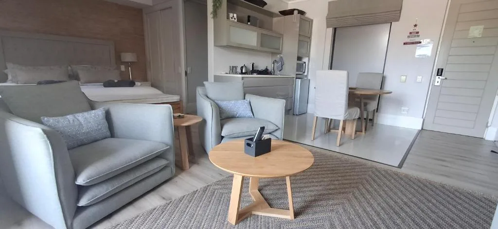 Modern lounge with gray armchairs, wooden table, kitchen and bedroom visible