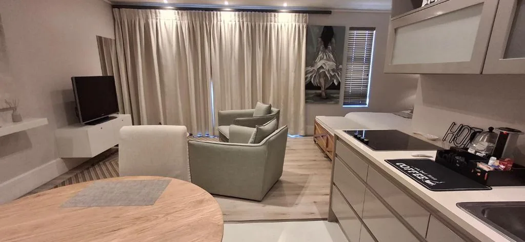 Modern living room with cream armchairs, television, and open-plan kitchen area