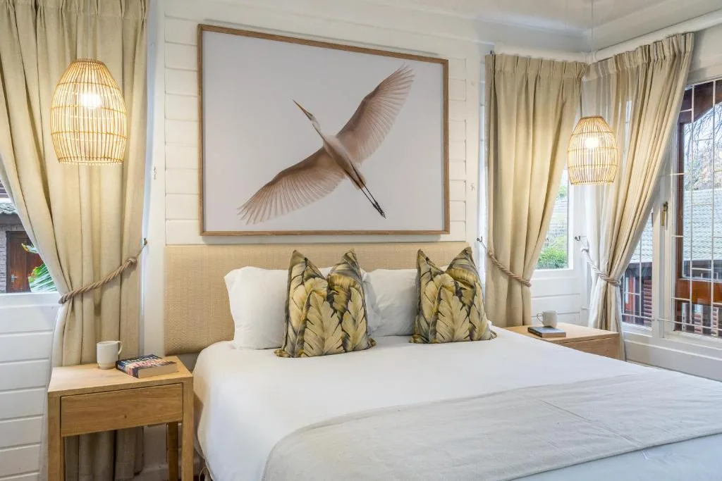 Bright bedroom with queen bed, botanical artwork, and cream curtains
