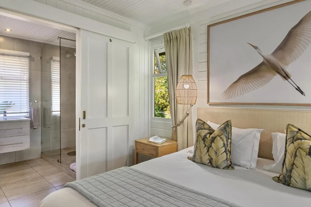 Bright bedroom with bed, en-suite bathroom visible, bird artwork, pendant light