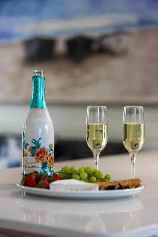Sparkling wine bottle with glasses, grapes, and crackers on white plate