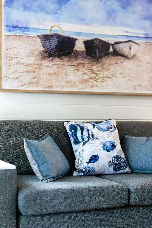 Gray sofa with blue cushions beneath coastal boat artwork