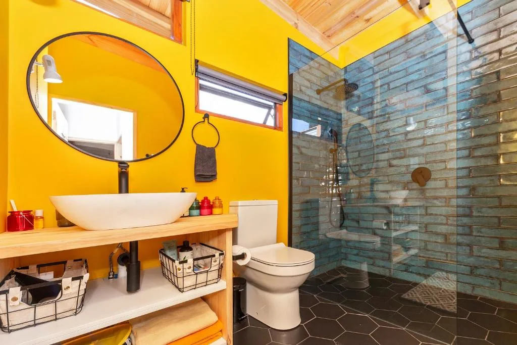 Bright yellow bathroom with round mirror, vessel sink, and walk-in shower