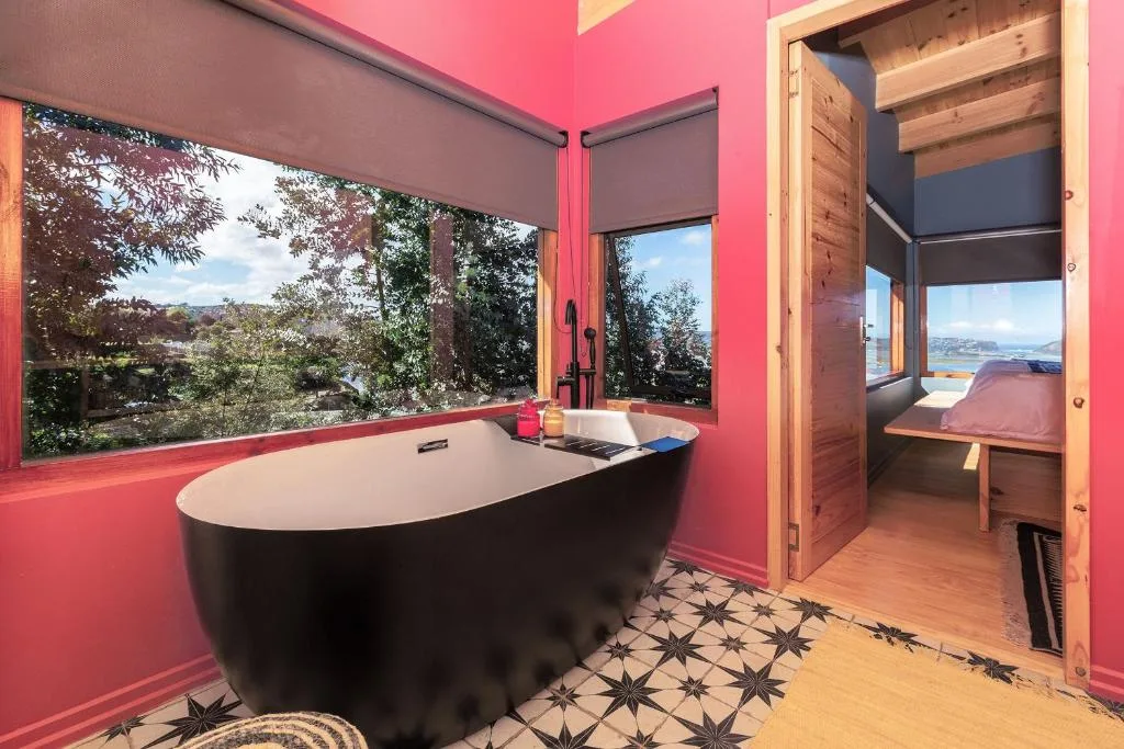 Modern black freestanding bathtub with vibrant pink walls and lagoon views