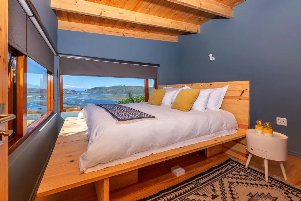 Modern bedroom with wooden bed frame overlooking lagoon water views through large windows