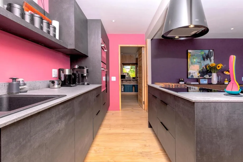 Modern kitchen with pink and purple walls, stainless steel appliances, and island counter