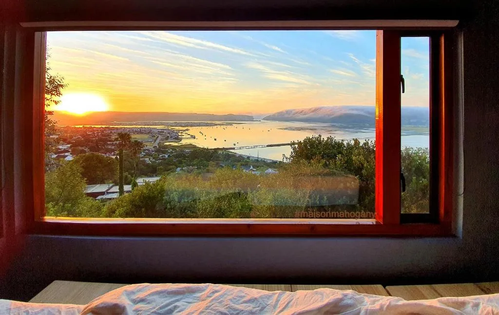 Sunset over Knysna Lagoon framed by red-trimmed bedroom window