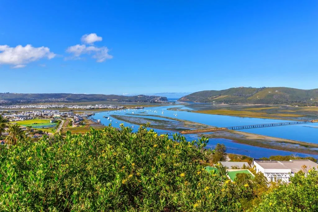 Panoramic lagoon view with blue water, bridge, and distant mountains under clear sky