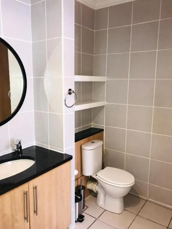 Modern bathroom with black vanity, round mirror, white toilet, and tiled walls