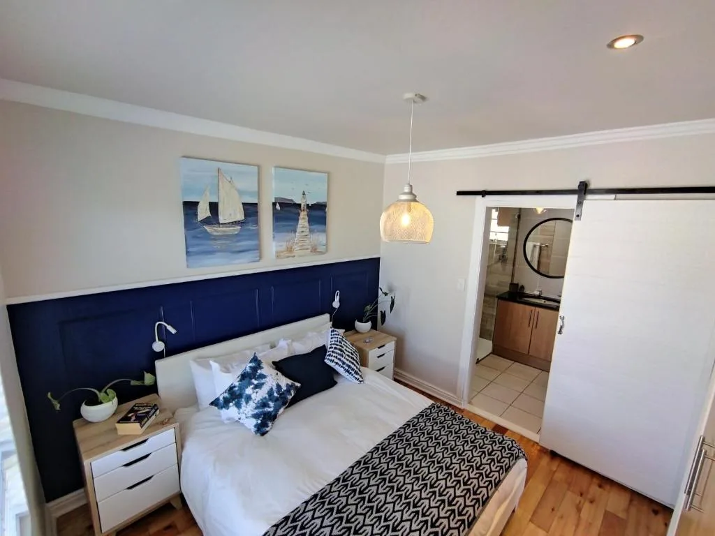 Modern bedroom with navy headboard, white bedding, nautical artwork, and ensuite bathroom
