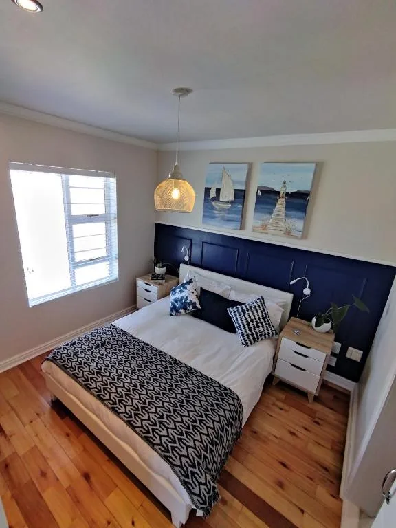 Modern bedroom with navy headboard, white bedding, wooden floor, pendant light