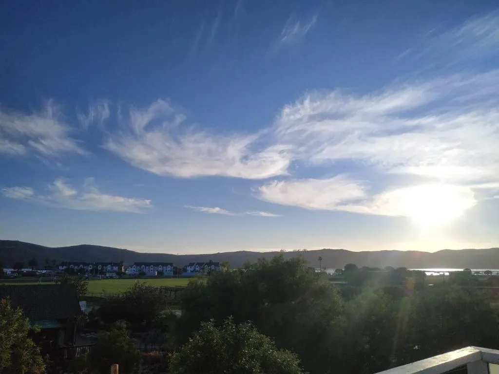 Scenic view of Knysna lagoon, mountains, and village buildings under blue sky