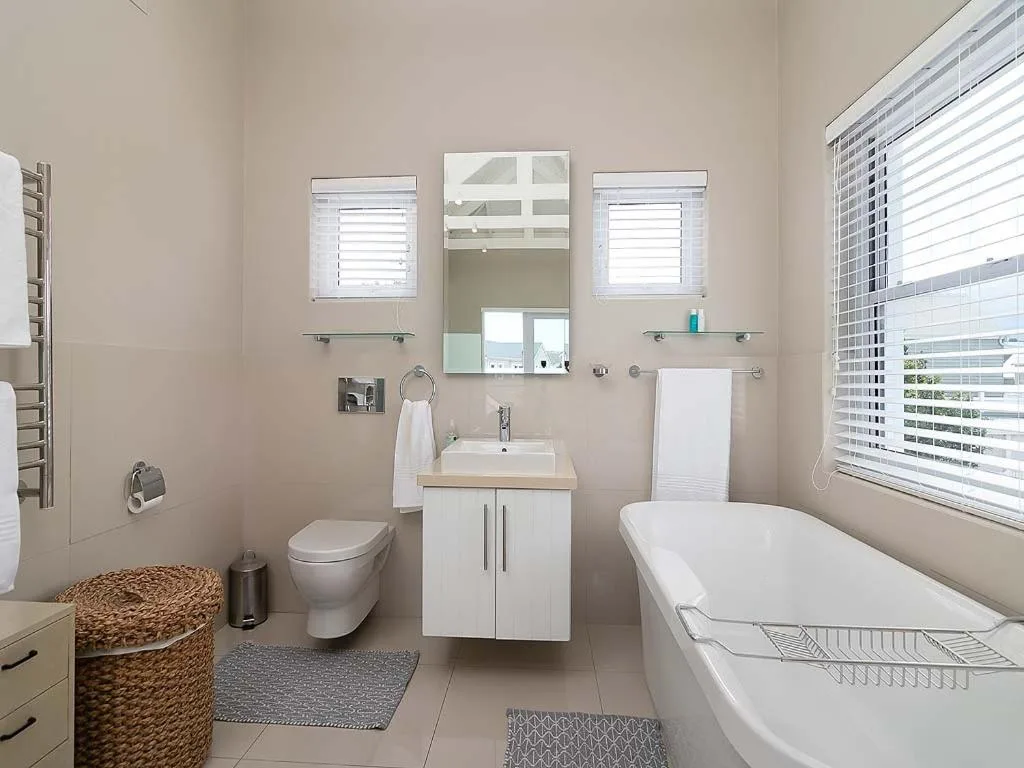 Bright modern bathroom with white vanity, bathtub, toilet, and mirror cabinet