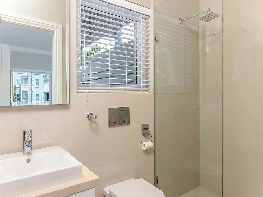 Modern bathroom with white vanity, glass shower enclosure, and window