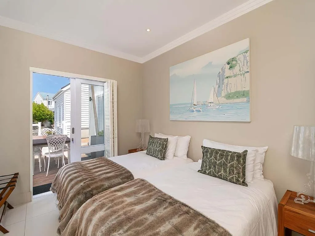 Bright bedroom with twin beds, nautical artwork, and deck access overlooking garden