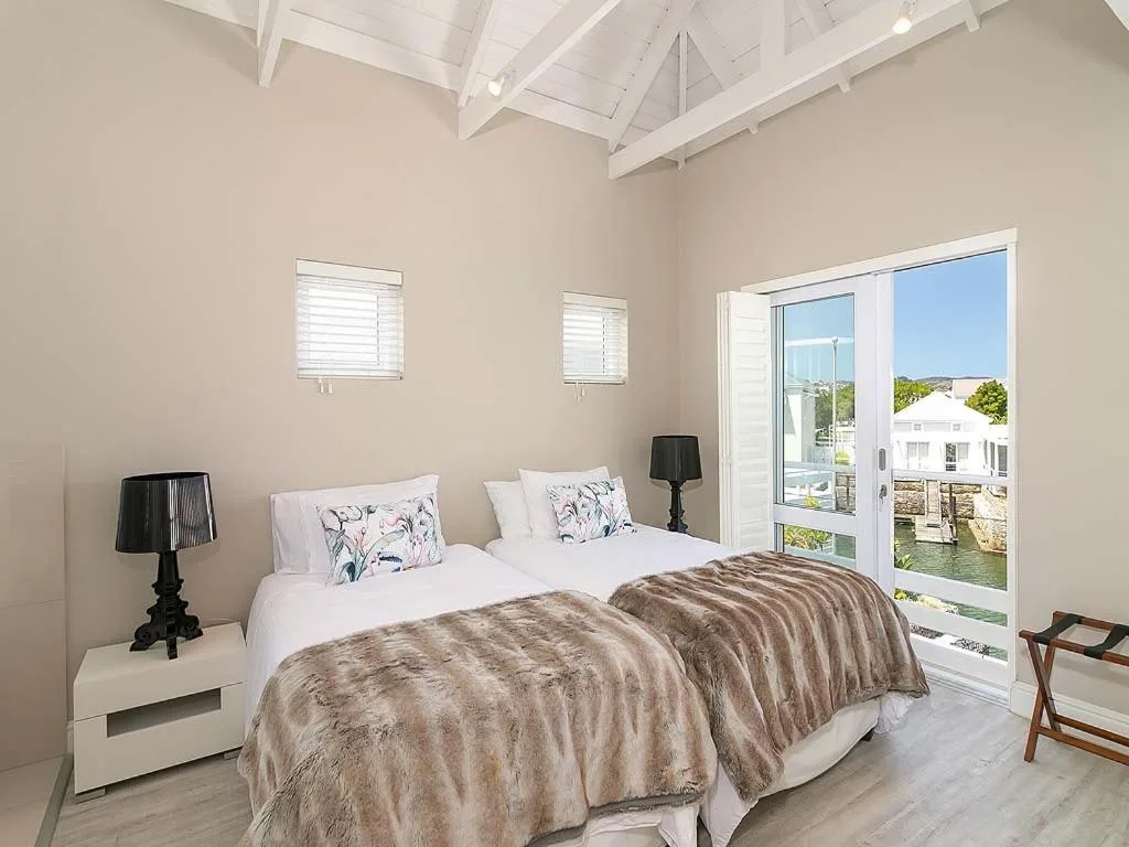 Bright bedroom with twin beds, modern furnishings, and glass doors overlooking water