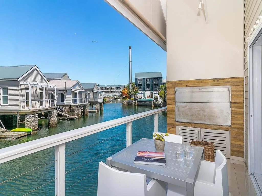 Waterfront deck with dining table overlooking blue canal and boathouses