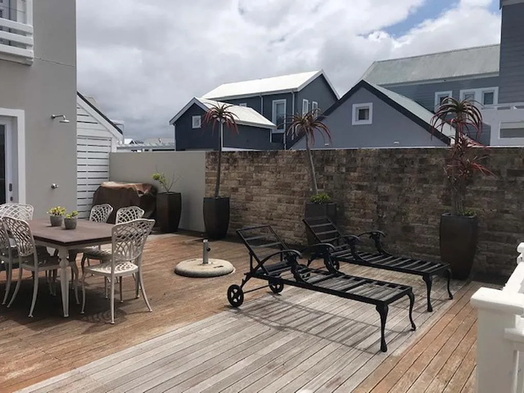 Spacious wooden deck with dining table, loungers, and stone wall boundary