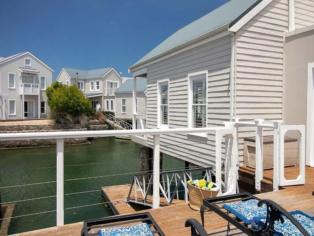 Wooden deck with white railings overlooking calm canal water and neighboring properties